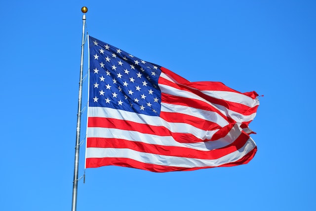 an american flag waves in the wind against the backdrop of a clear blue sky
